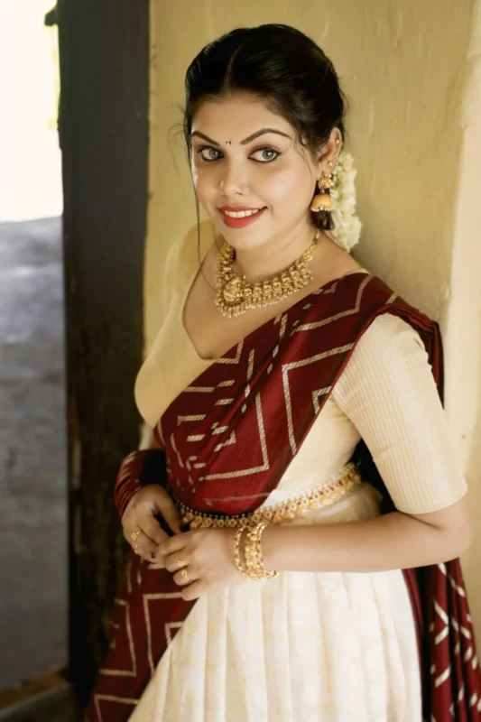 Designer cream ethnic lehenga with maroon dupatta and gold jewelry – traditional festive outfit for women.